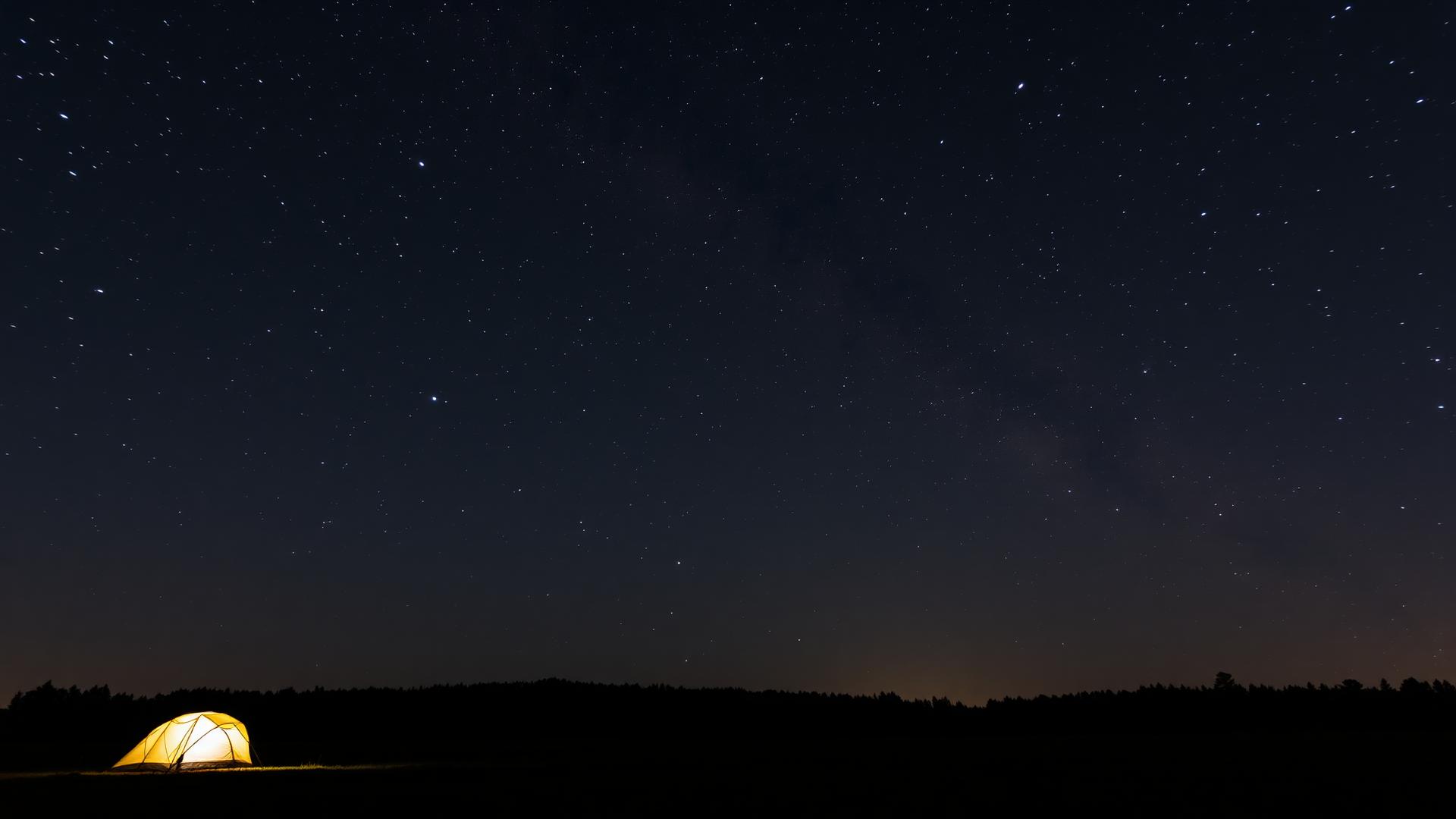 Night sky over a quiet field with a softly glowing tent